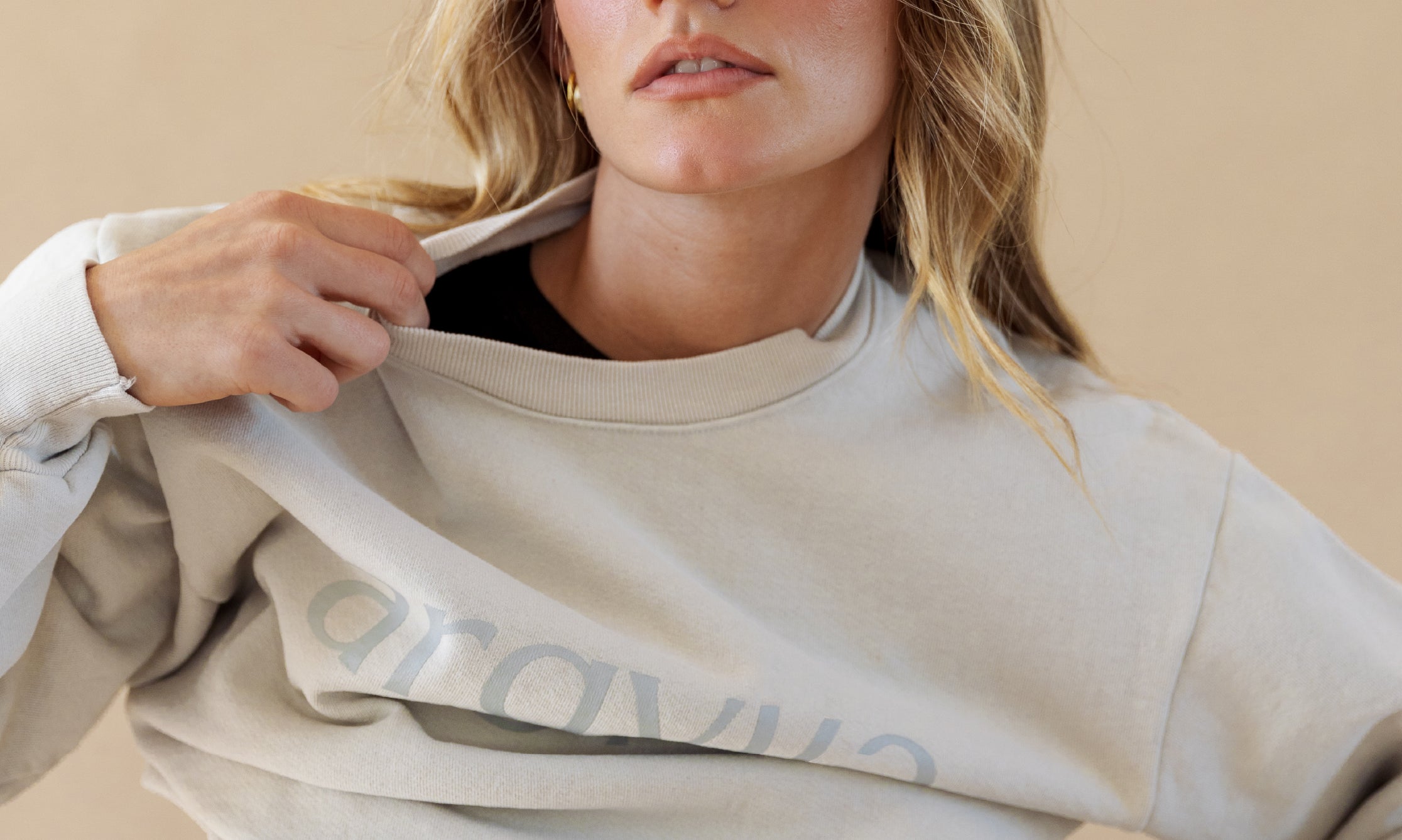 Woman wearing a light gray sweatshirt with a brand logo on a beige background