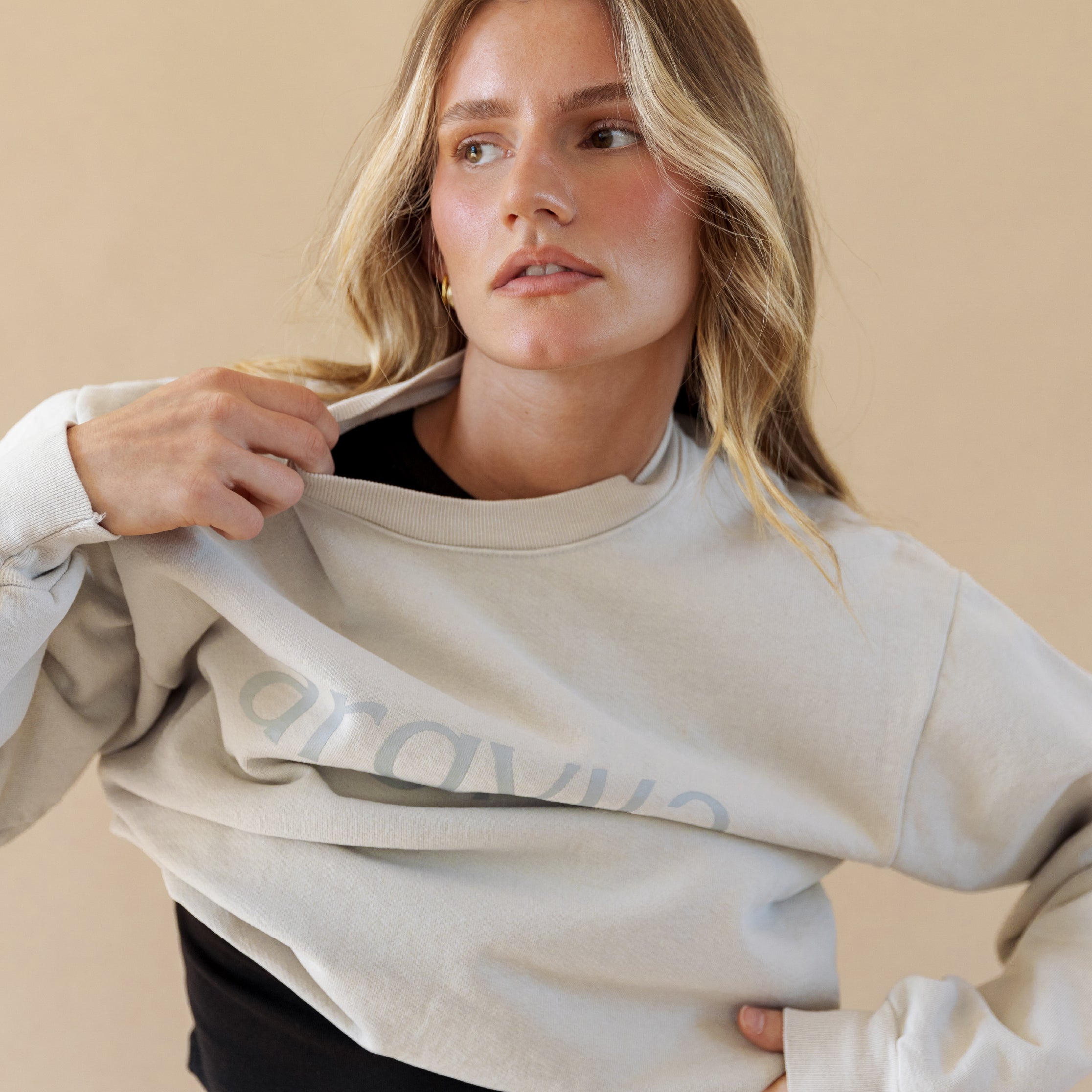 Woman wearing a light gray sweatshirt with a brand logo on a beige background