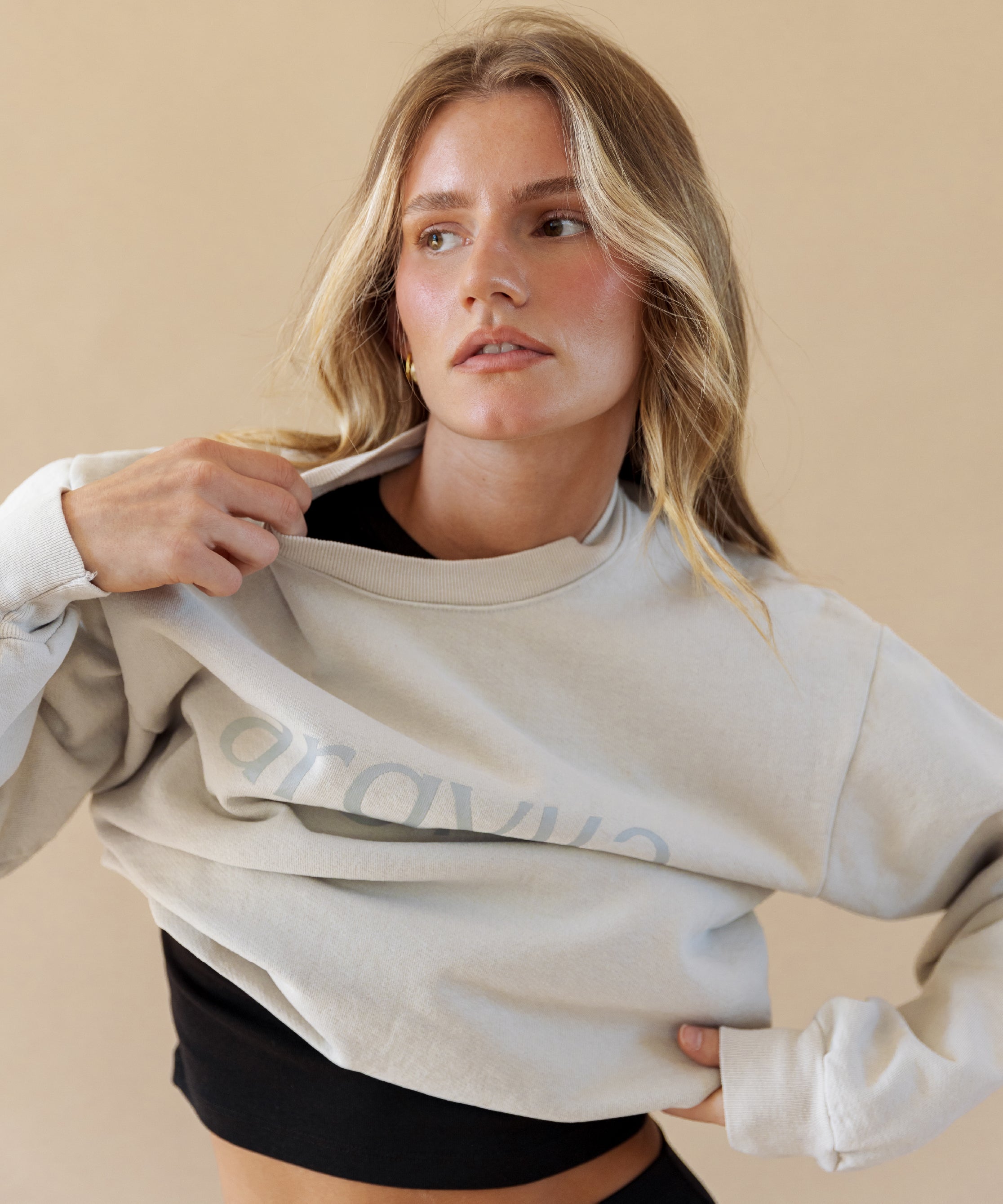 Woman wearing a light gray sweatshirt with a brand logo on a beige background