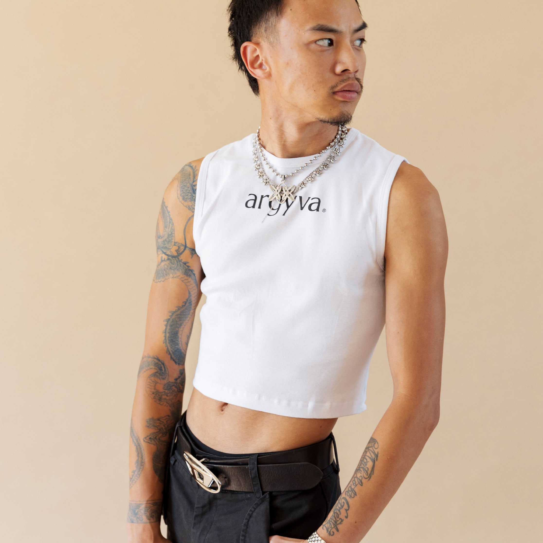 Man wearing a white sleeveless shirt with 'ardya' branding on a beige background