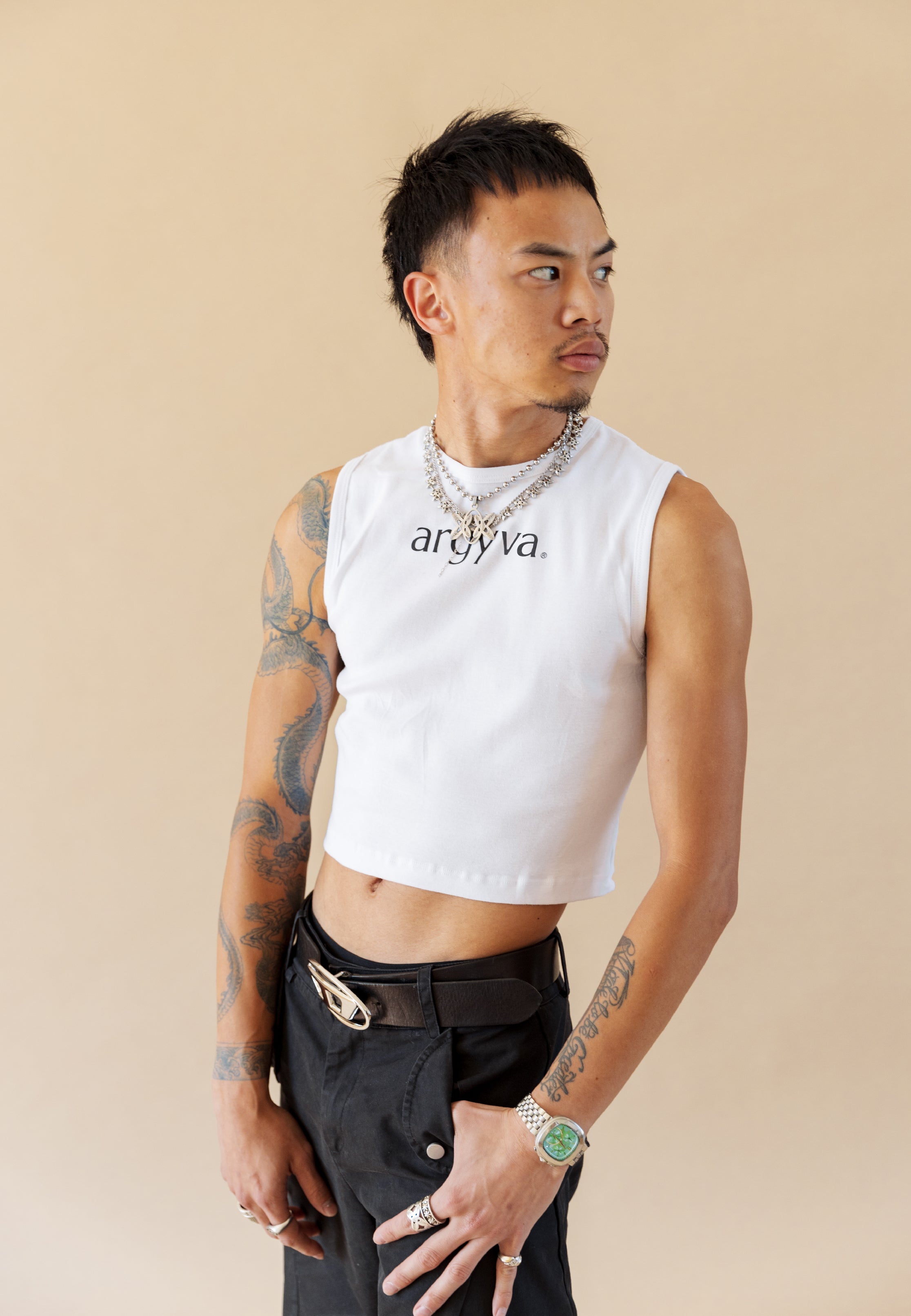 Man wearing a white sleeveless shirt with 'ardya' branding on a beige background